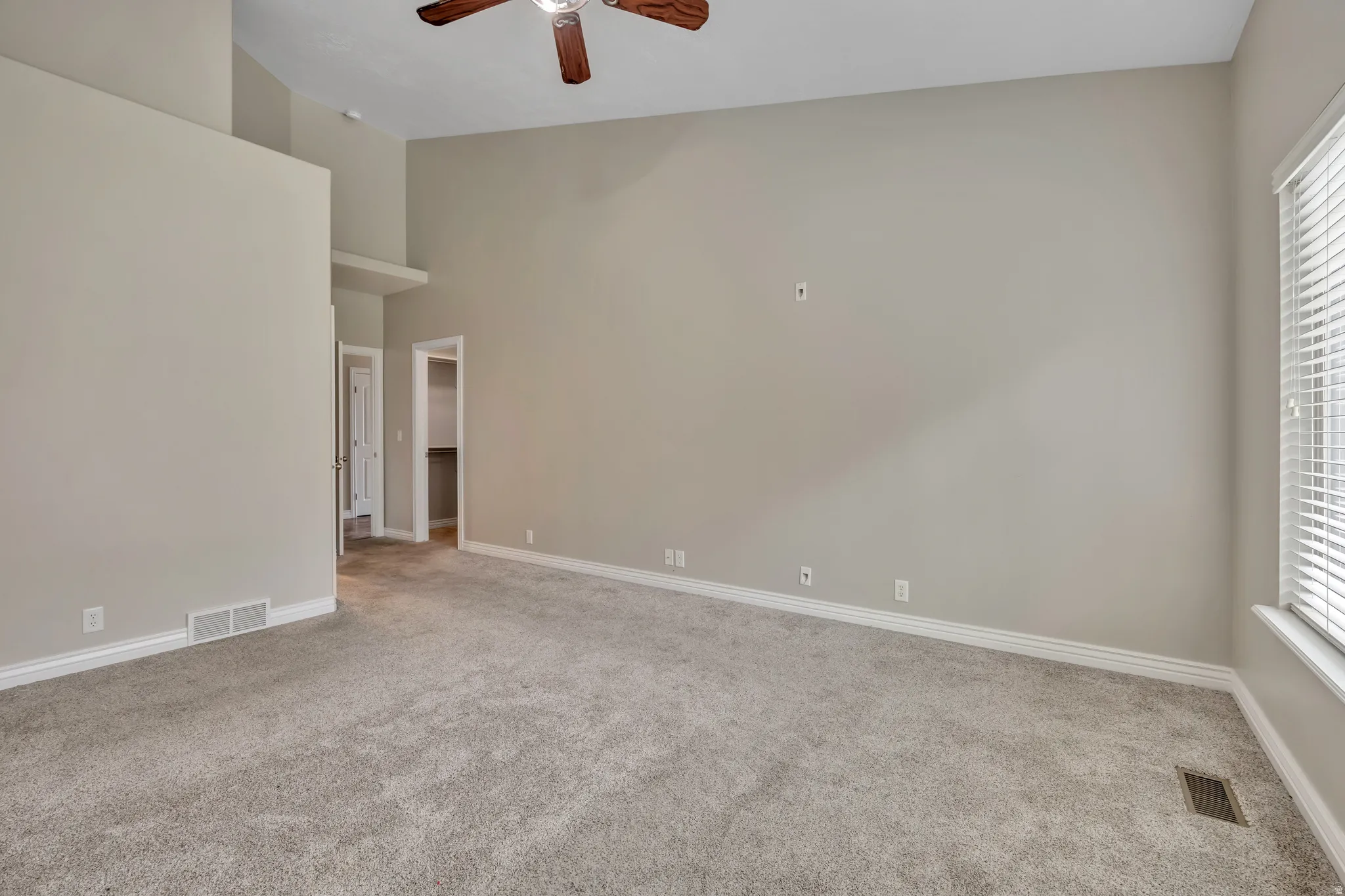 Unfurnished room with ceiling fan, light colored carpet, plenty of natural light, and a high ceiling