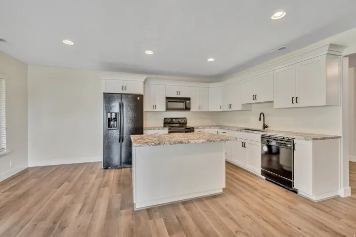 Kitchen with black appliances, white cabinetry, a kitchen island, light stone counters, and recessed lighting