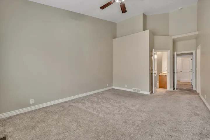 Unfurnished bedroom featuring ensuite bath, light colored carpet, ceiling fan, and a high ceiling