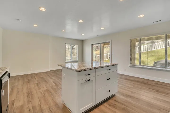 Kitchen featuring a center island, white cabinetry, light stone counters, stainless steel dishwasher, and light wood finished floors