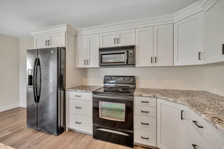 Kitchen with black appliances, white cabinetry, light wood-type flooring, and light stone counters