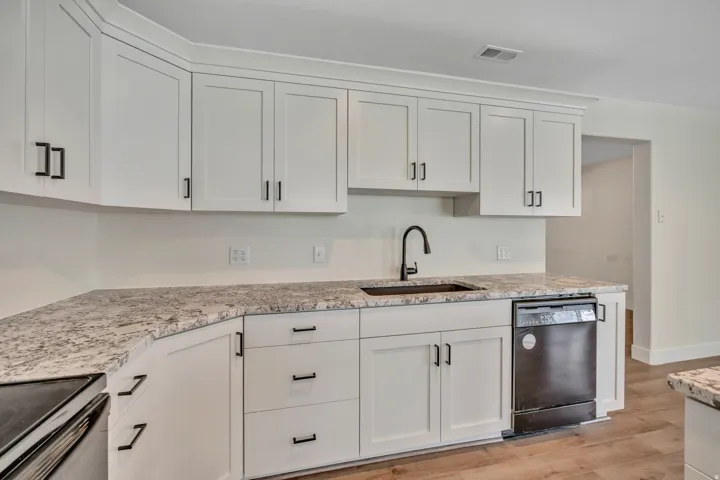 Kitchen with white cabinets, black appliances, light stone countertops, and light wood-type flooring