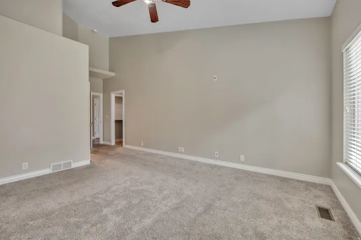 Unfurnished room with ceiling fan, light colored carpet, plenty of natural light, and a high ceiling