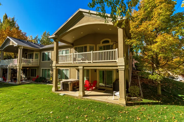 Rear view of house featuring a patio, stucco siding, a lawn, and a balcony