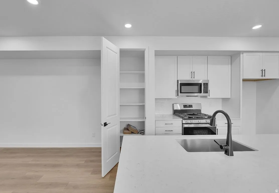 Kitchen with appliances with stainless steel finishes, recessed lighting, white cabinets, light wood-style flooring, and light stone countertops
