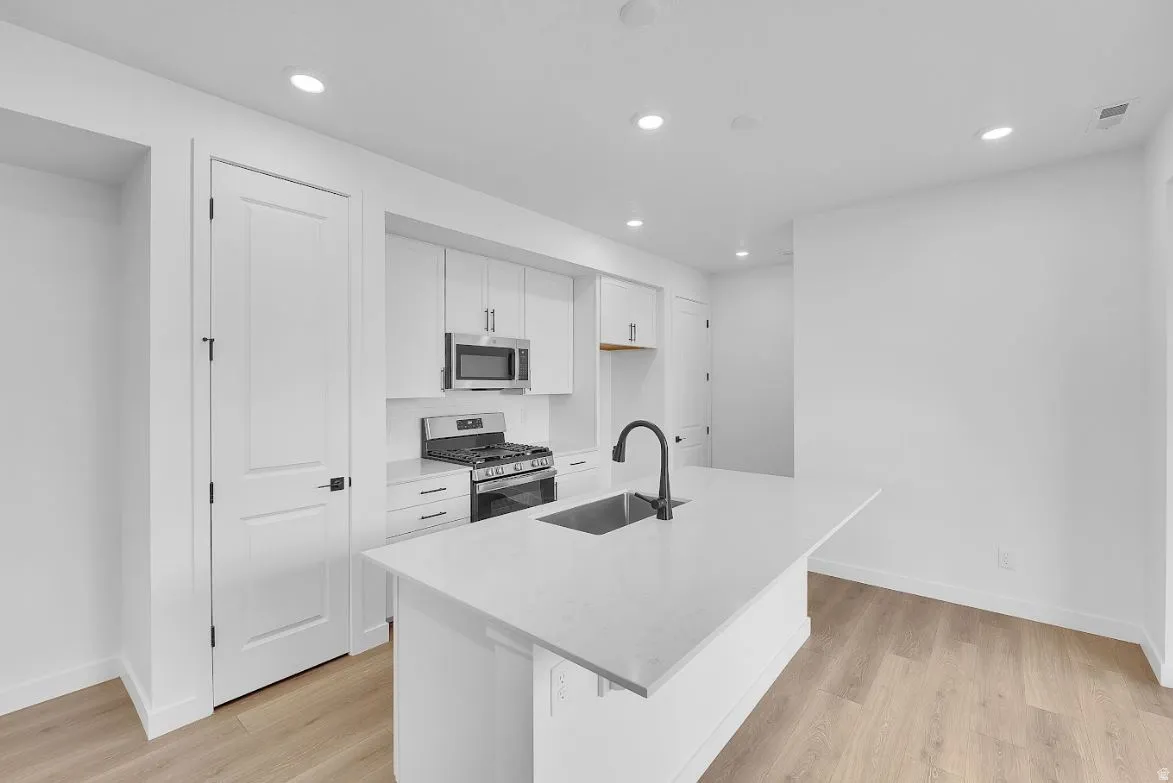 Kitchen with white cabinets, stainless steel appliances, an island with sink, light wood finished floors, and recessed lighting