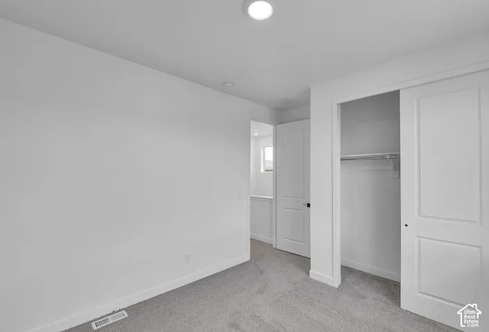 Unfurnished bedroom with light colored carpet and a closet