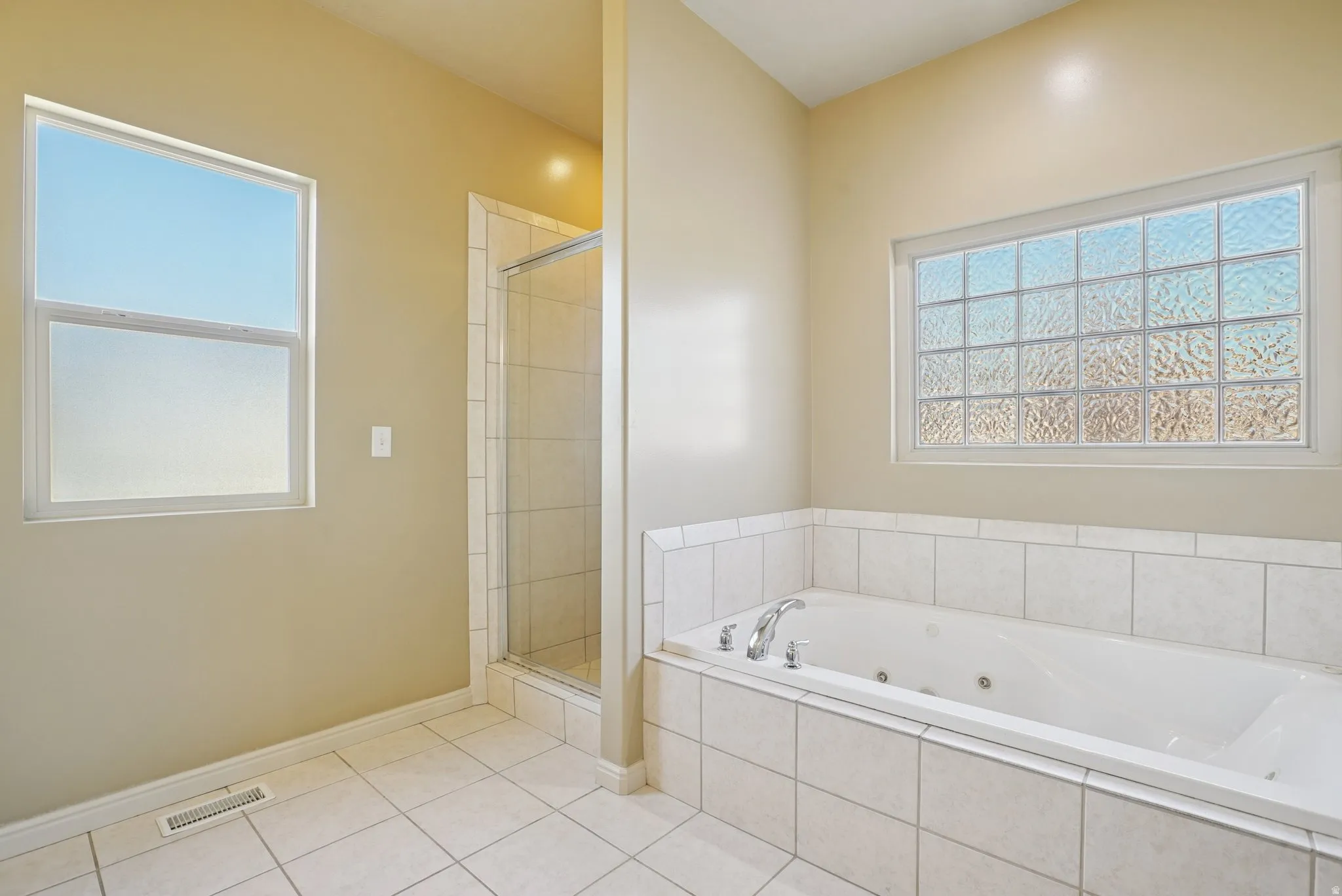 Bathroom with a whirlpool tub, healthy amount of natural light, a stall shower, and light tile patterned floors