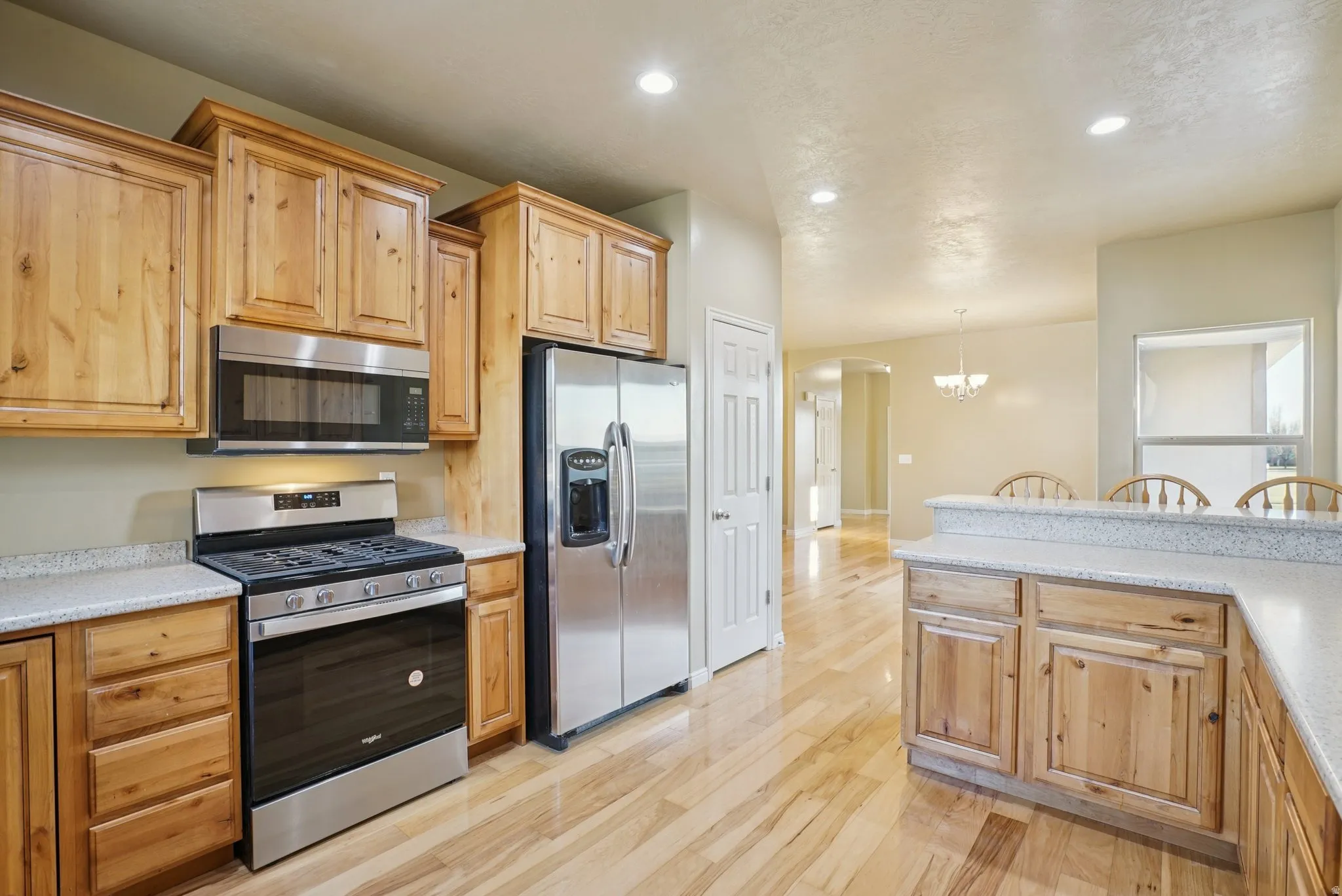 Kitchen with stainless steel appliances, arched walkways, light wood finished floors, recessed lighting, and a chandelier