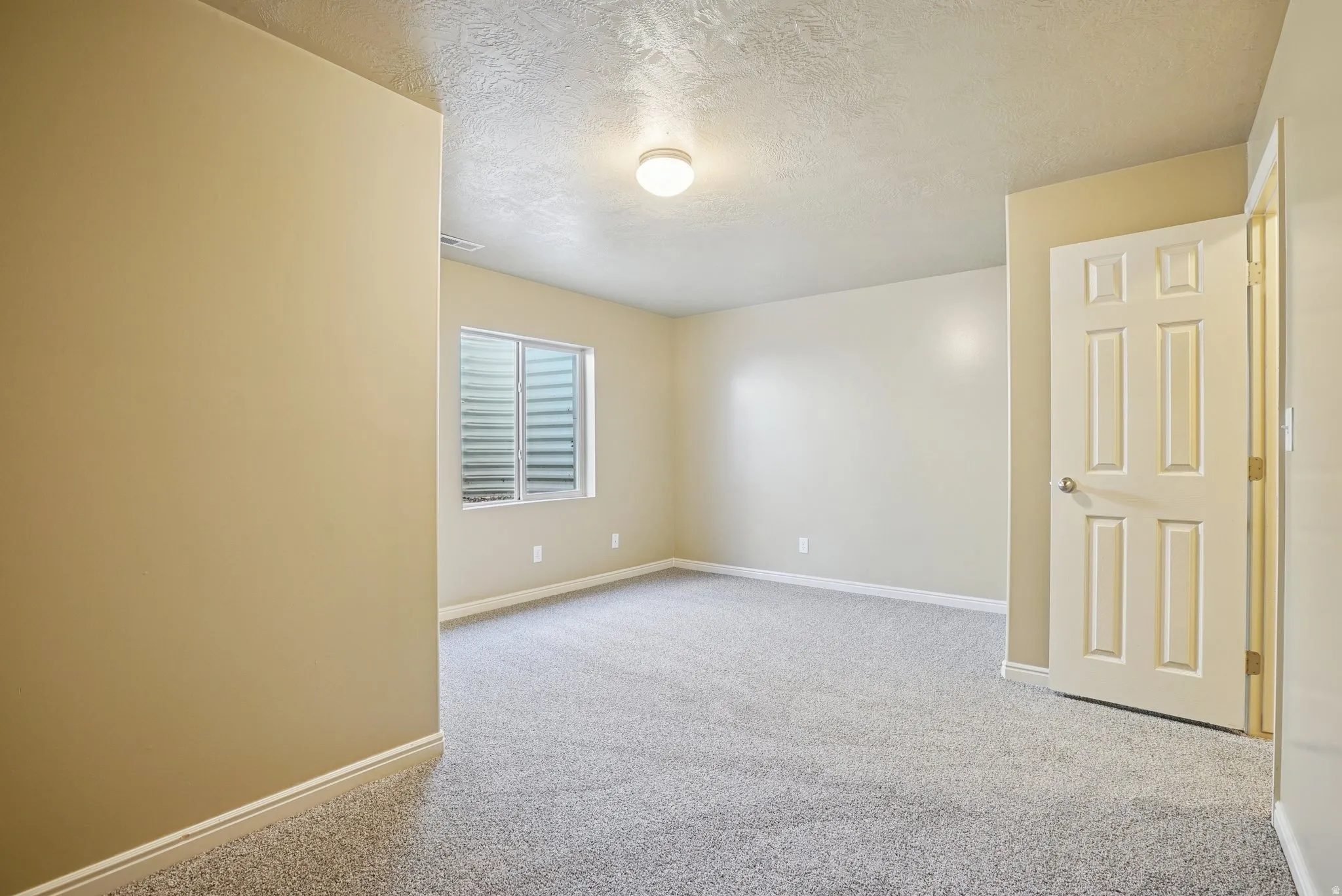 Empty room featuring a textured ceiling and light colored carpet