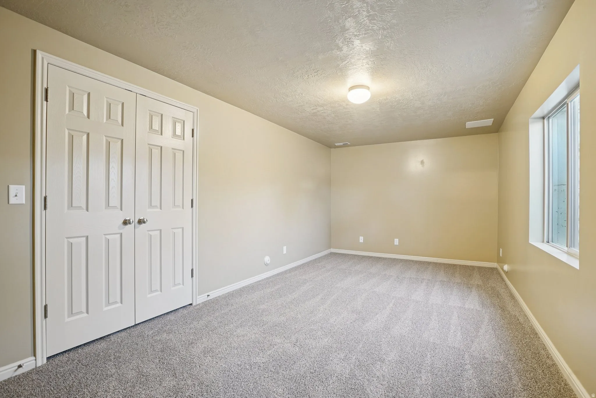 Unfurnished bedroom with a textured ceiling, light carpet, and a closet