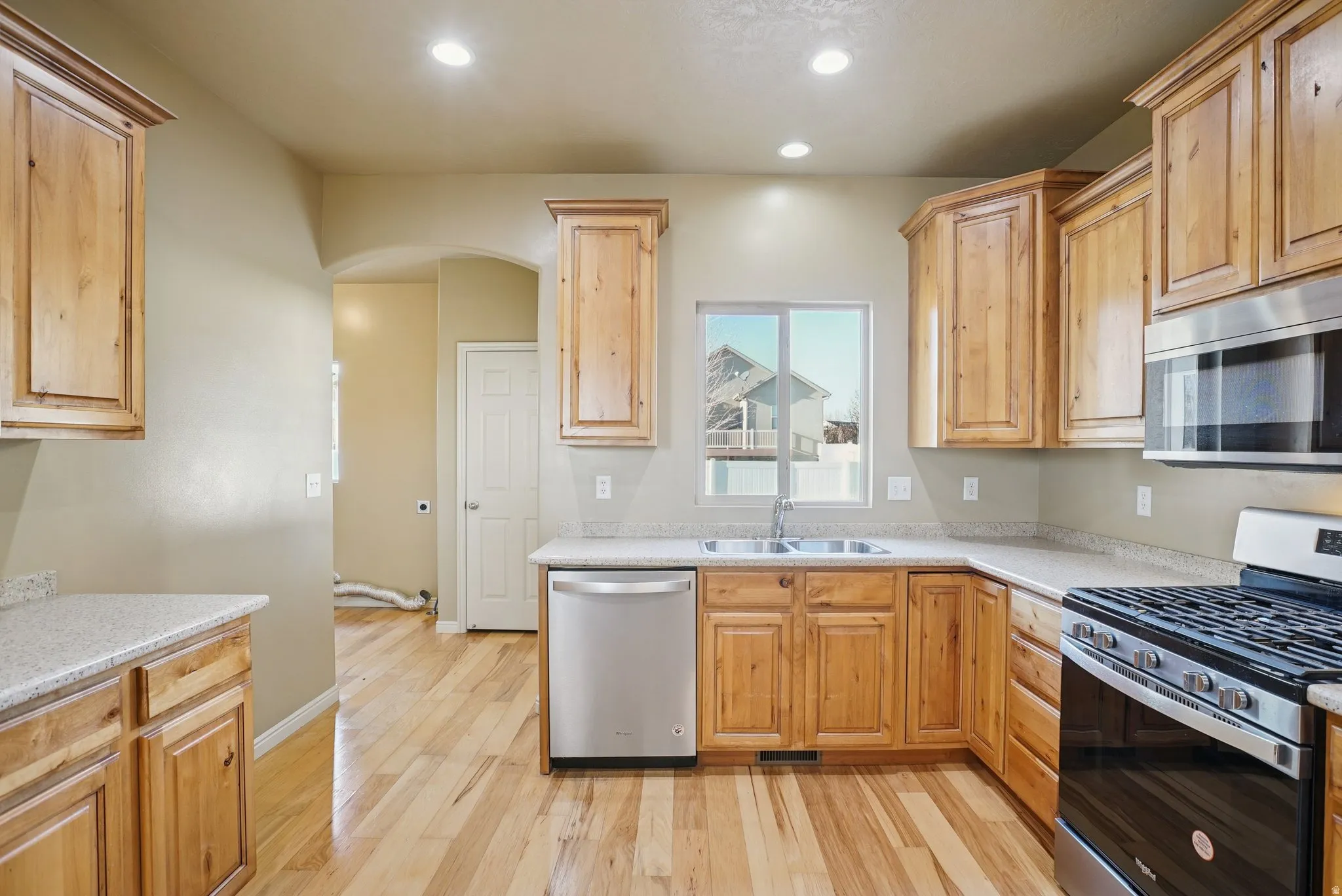 Kitchen featuring stainless steel appliances, light wood-style flooring, arched walkways, recessed lighting, and light stone countertops
