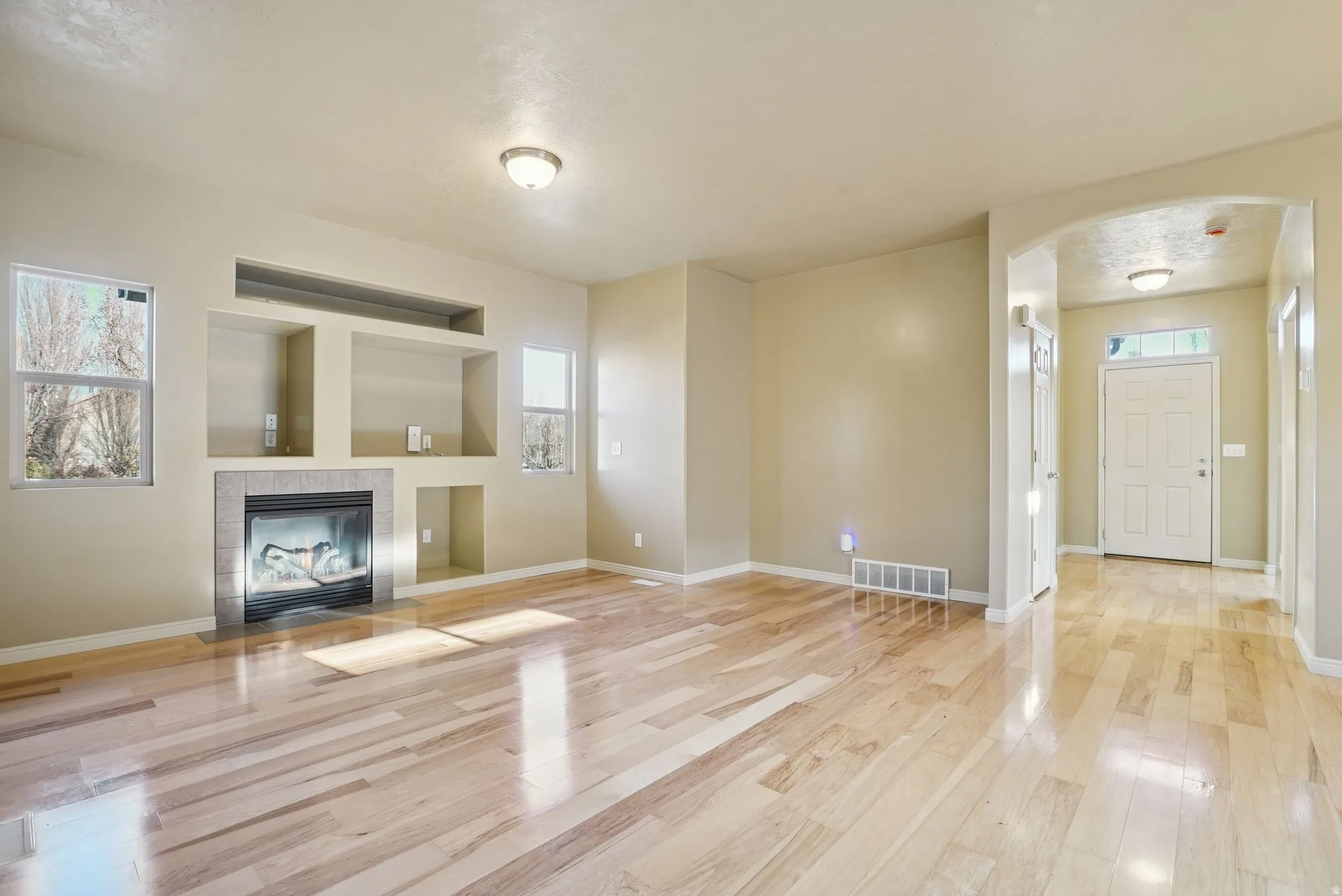 Unfurnished living room featuring arched walkways, light wood-style floors, a fireplace, and built in features