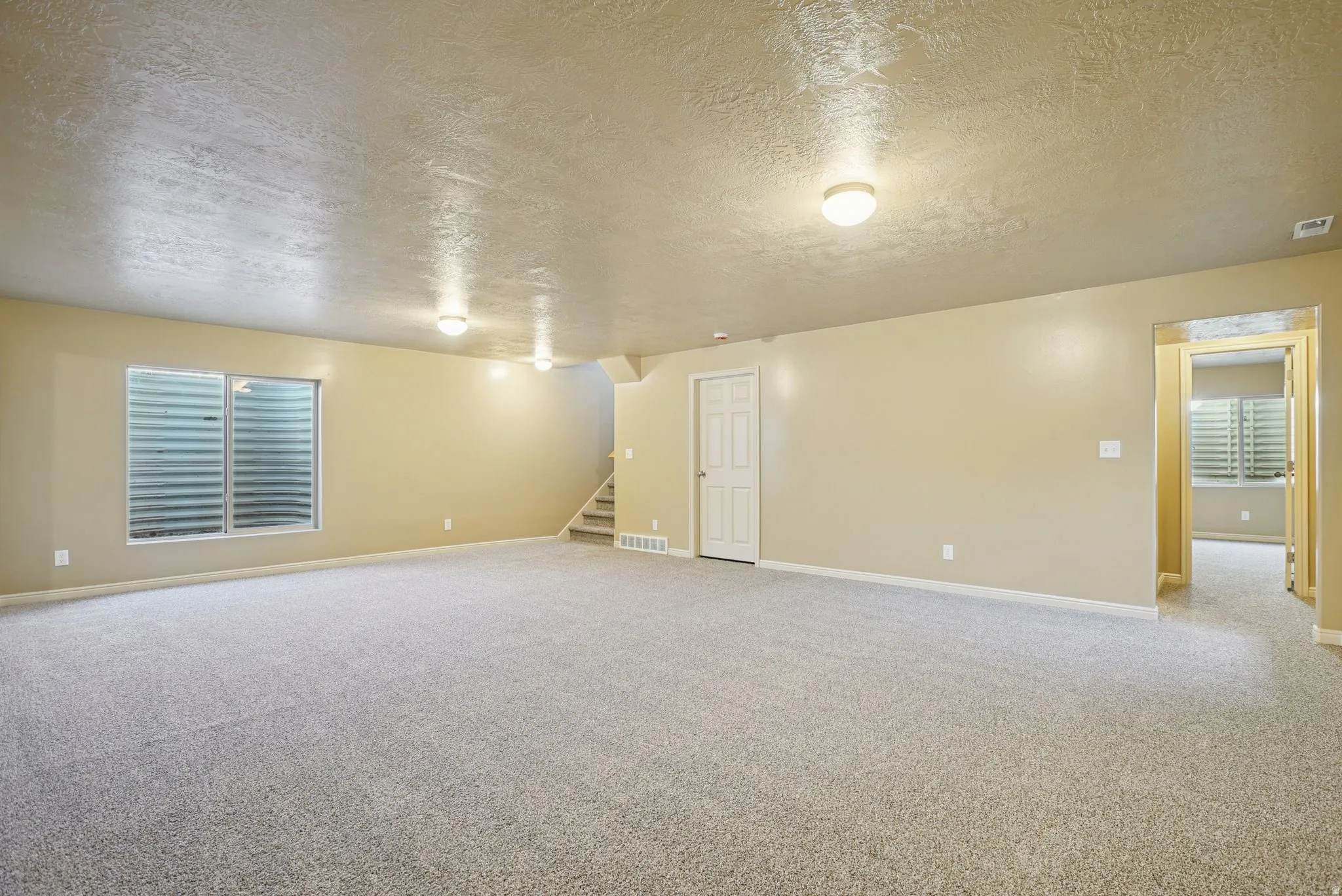 Unfurnished room featuring a textured ceiling, light carpet, and stairway