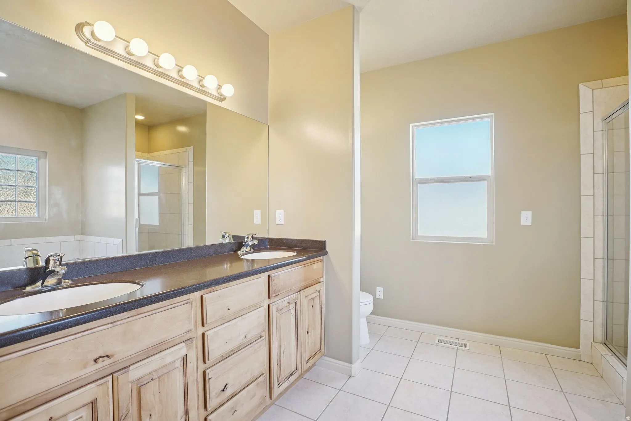 Bathroom with double vanity, a stall shower, and light tile patterned flooring
