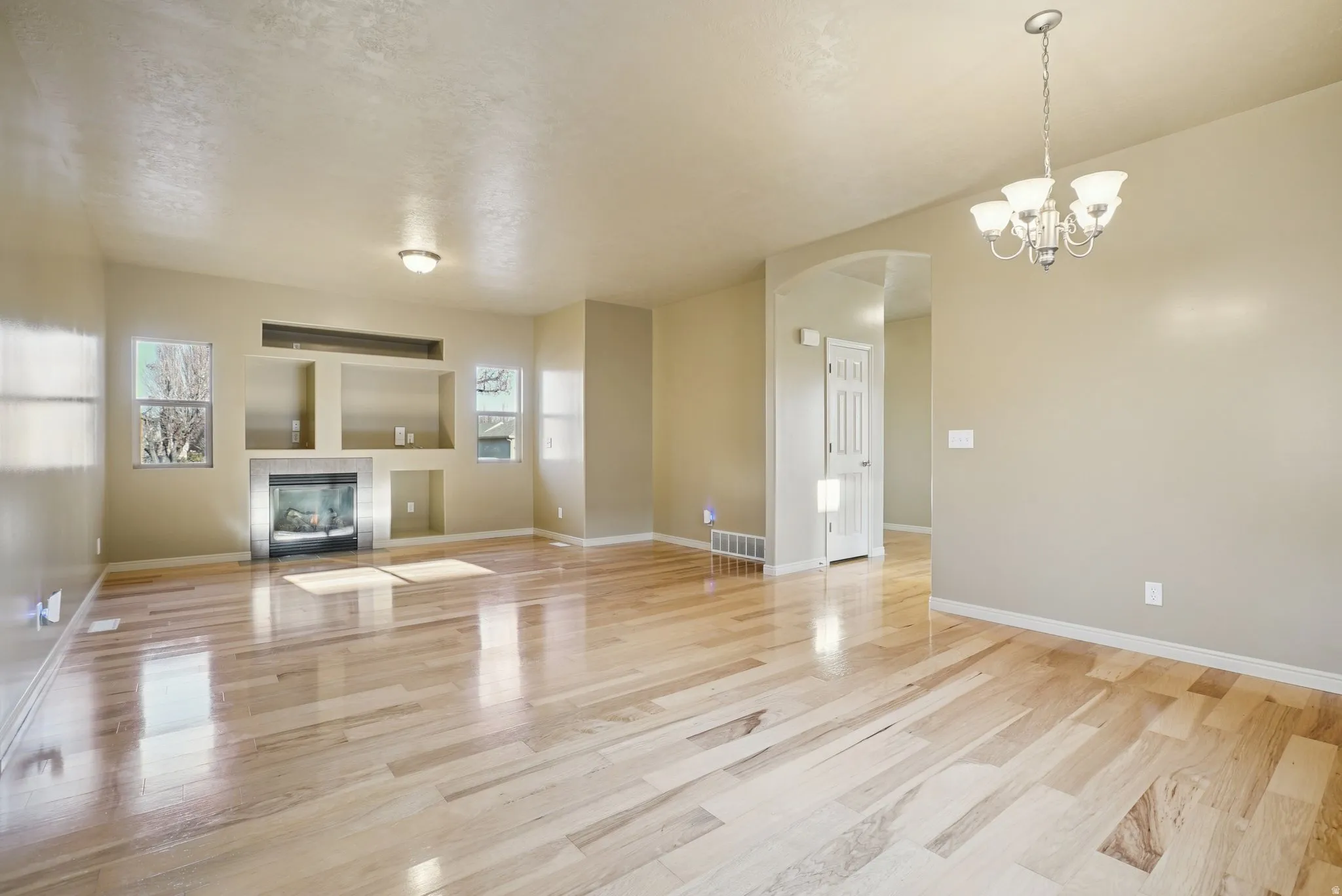 Unfurnished living room with arched walkways, a chandelier, a tile fireplace, and light wood finished floors