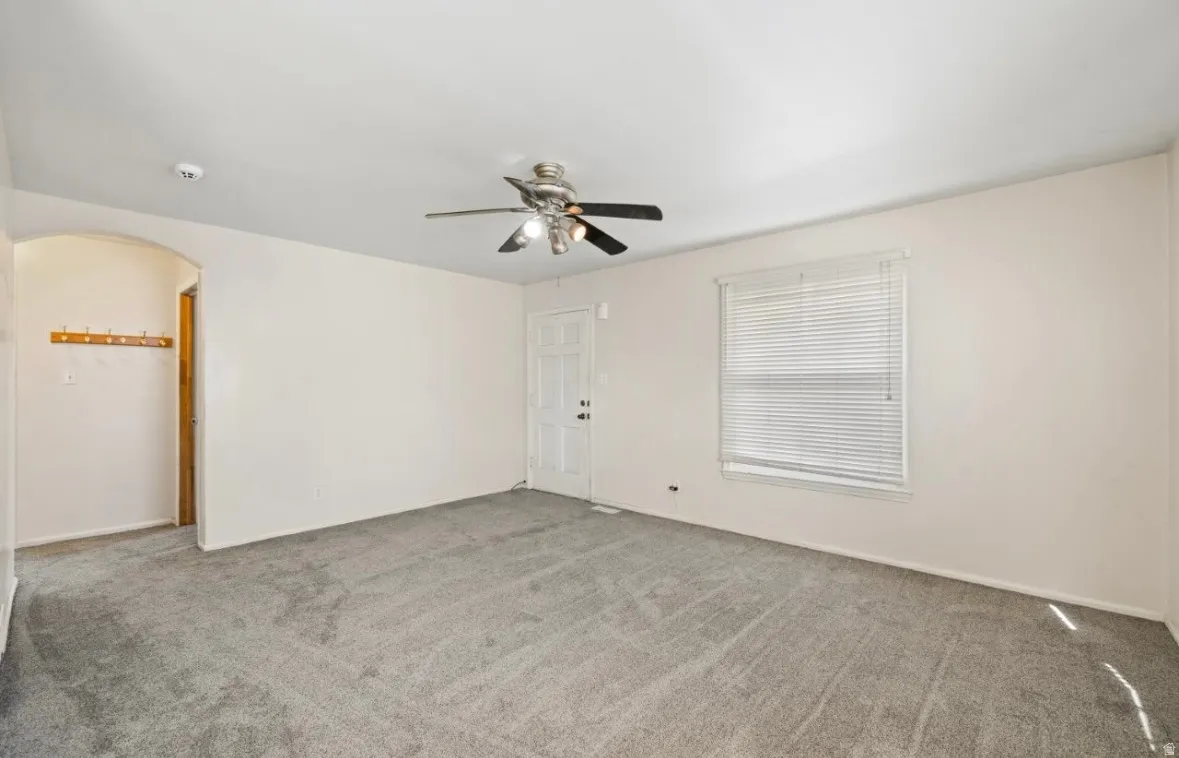 Empty room with carpet, arched walkways, and ceiling fan
