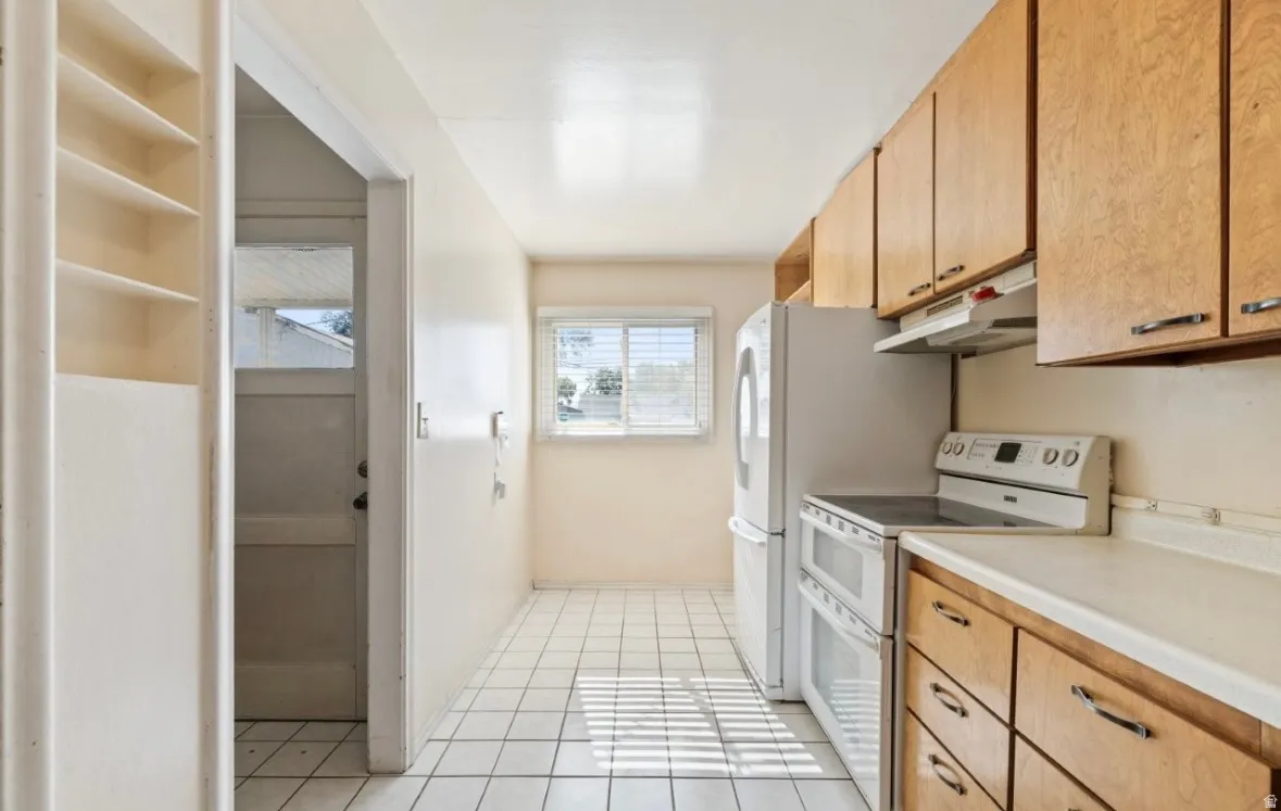 Kitchen with double oven range, light countertops, light tile patterned flooring, under cabinet range hood, and brown cabinets