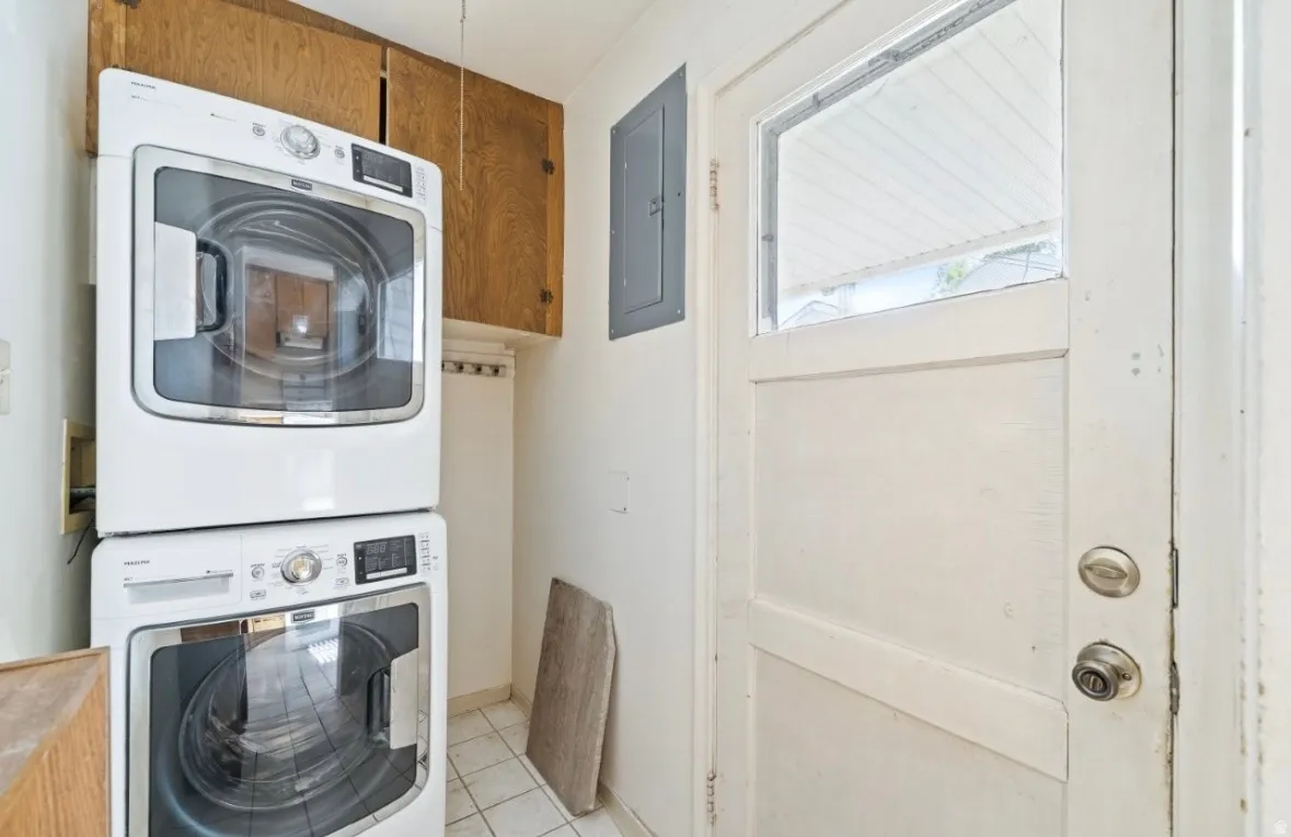 Laundry room with electric panel, stacked washer / drying machine, and light tile patterned floors