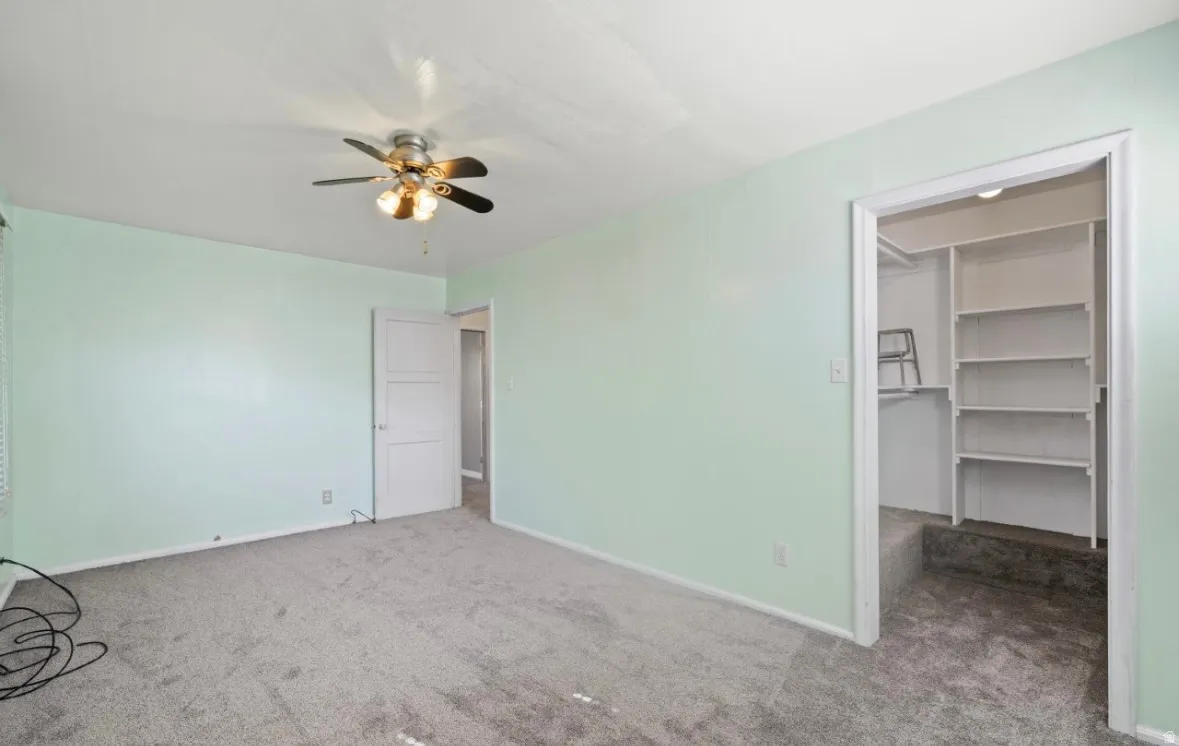 Unfurnished bedroom featuring a spacious closet, carpet flooring, and a ceiling fan