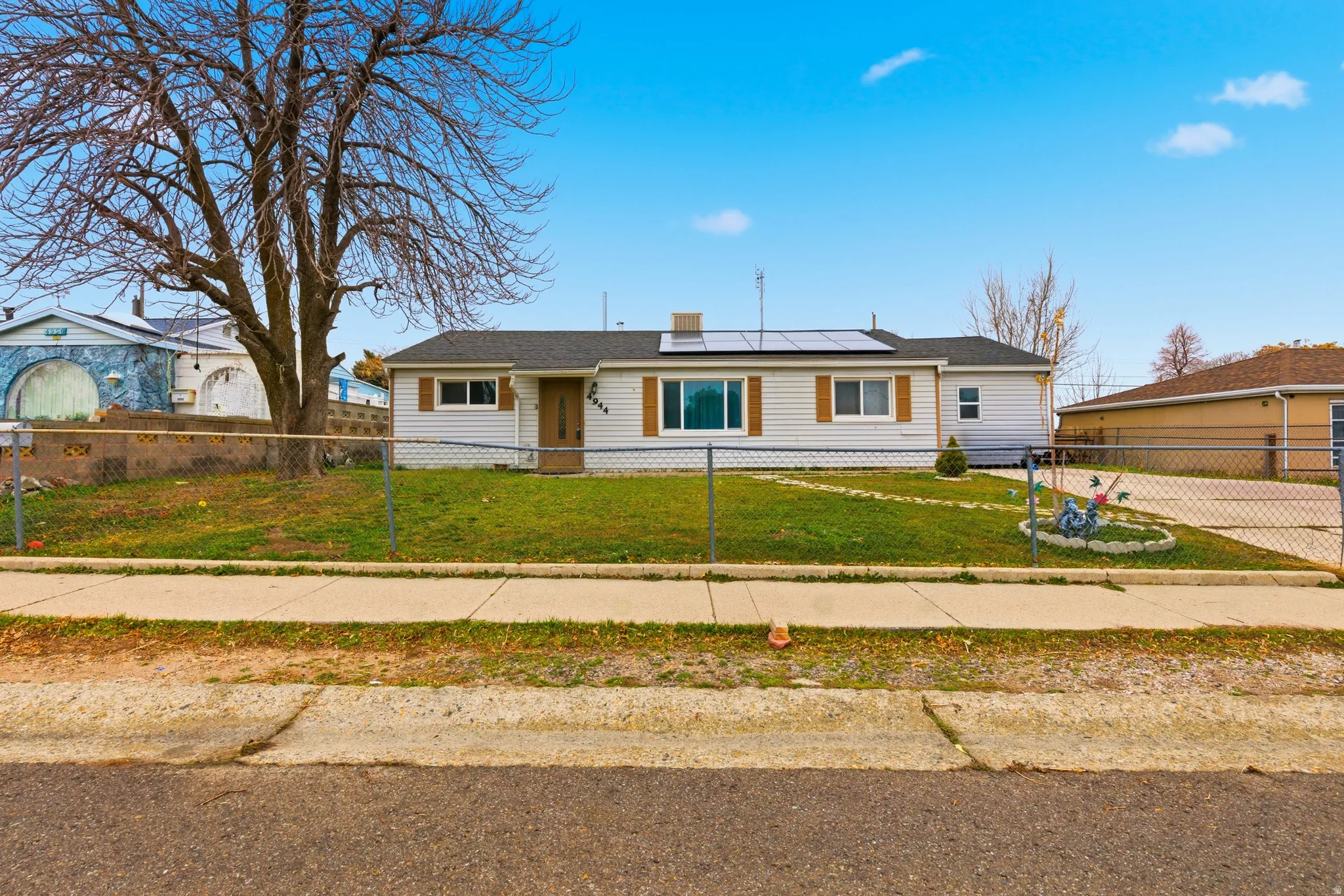 Single story home with solar panels and a fenced front yard