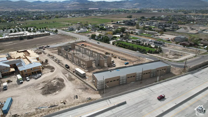 Aerial perspective of a development site featuring multi-unit commercial structures in various stages of construction, situated on a prominent corner lot with direct road access and mountain range backdrop