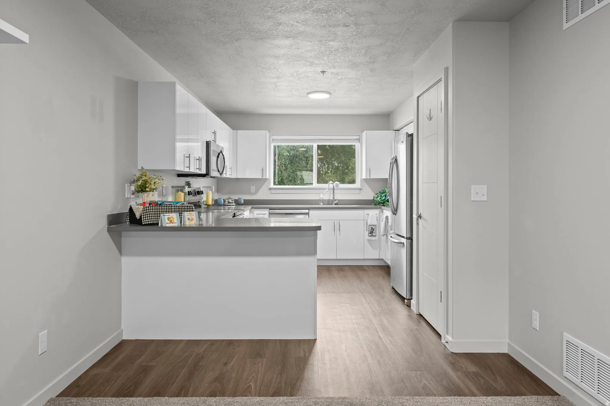 Kitchen featuring white cabinets, a peninsula, stainless steel appliances, wood finished floors, and a textured ceiling
