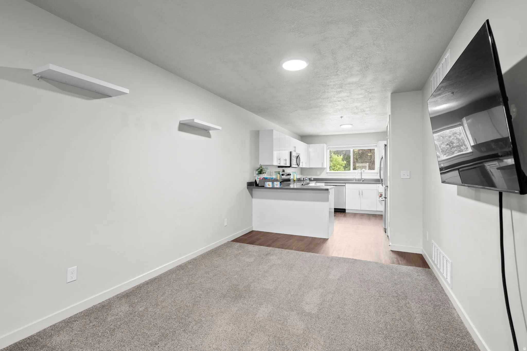 Kitchen with white cabinets, light colored carpet, open floor plan, a textured ceiling, and dark countertops
