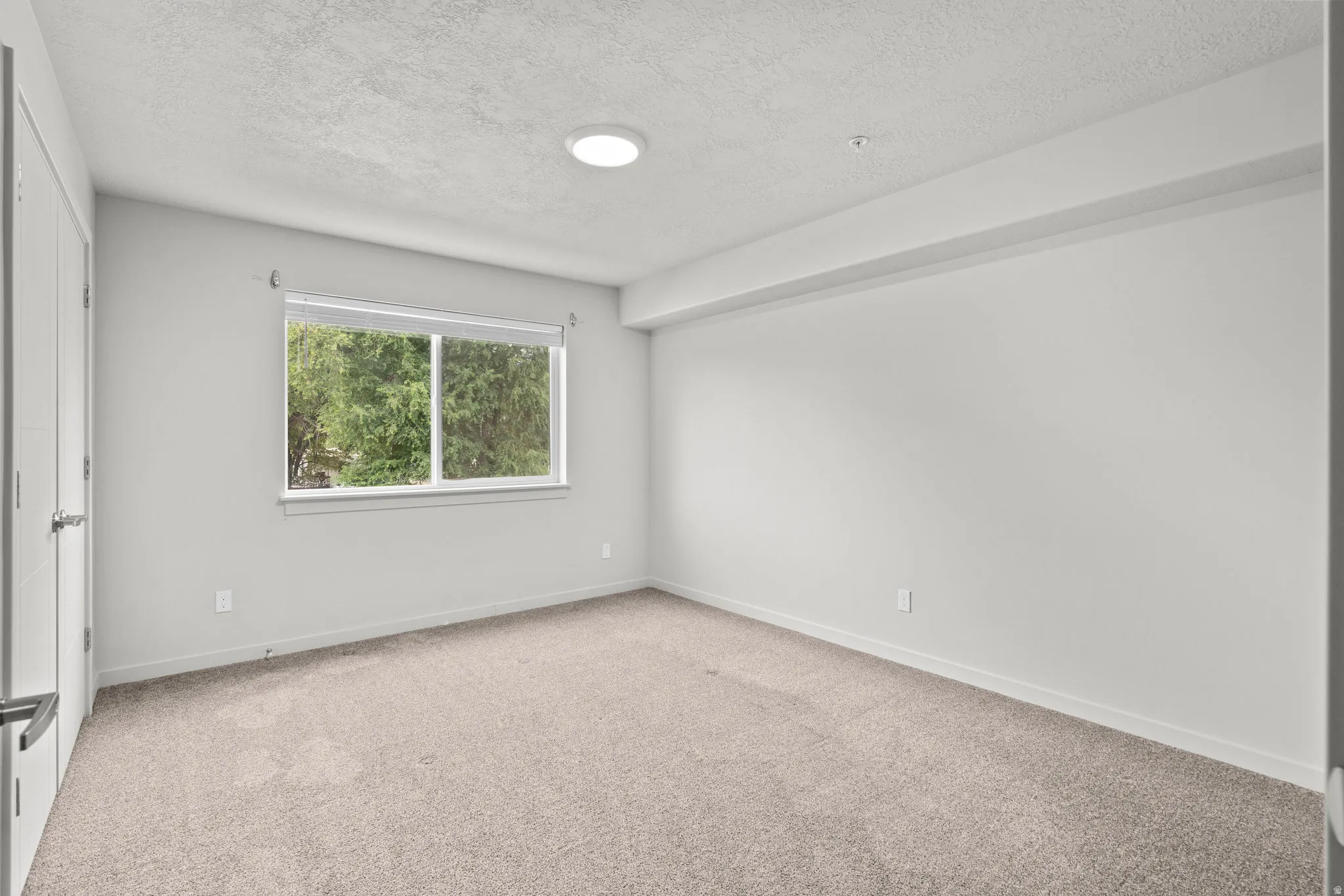 Empty room with light colored carpet and a textured ceiling