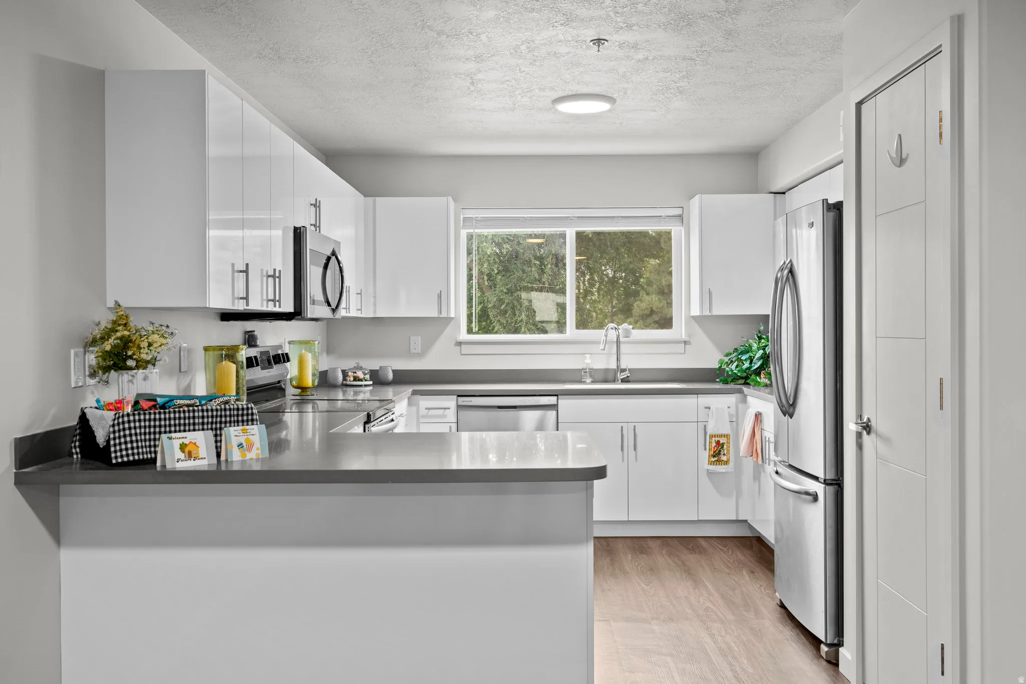 Kitchen with a peninsula, stainless steel appliances, white cabinets, a textured ceiling, and light wood-style floors