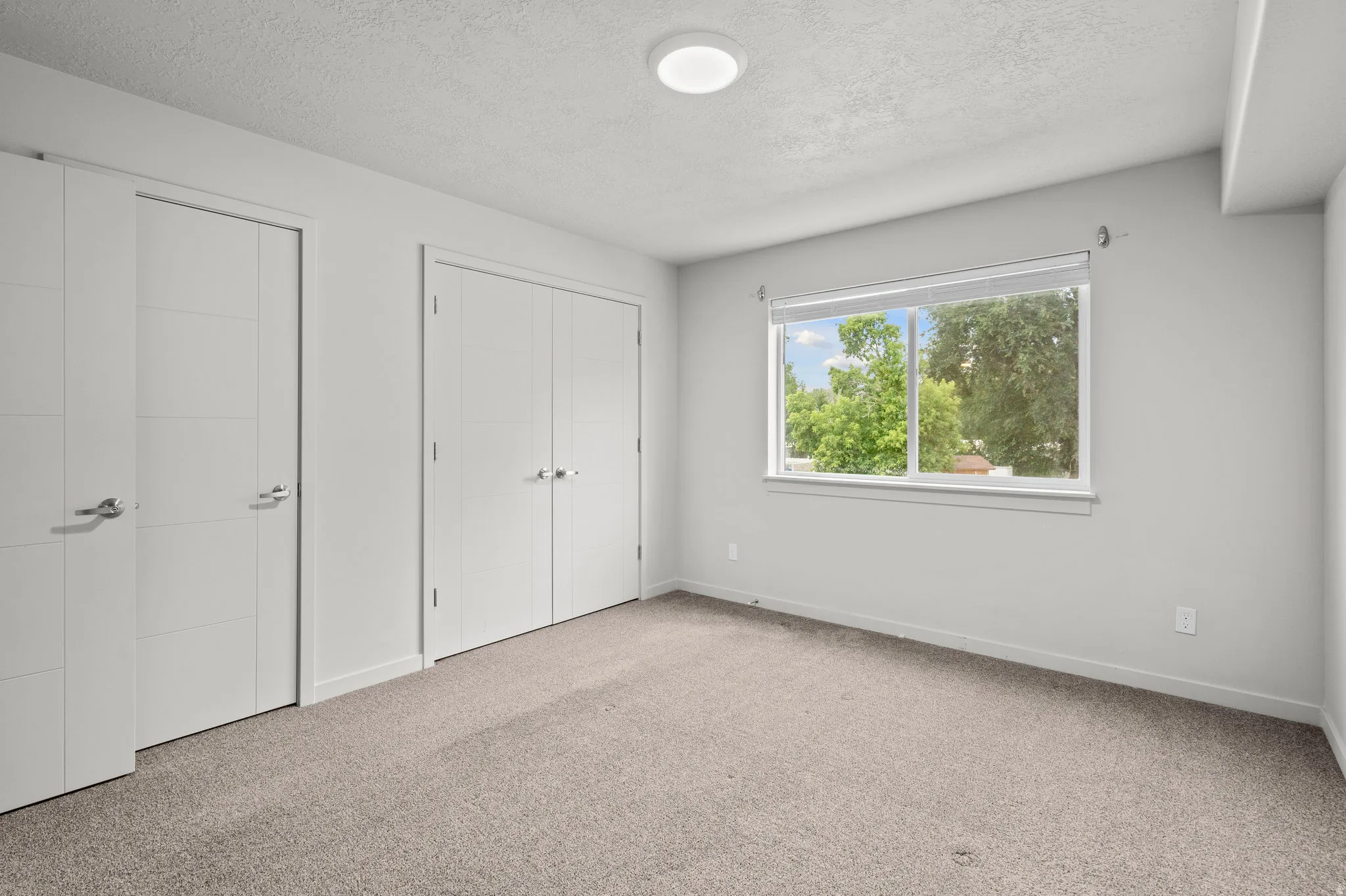 Unfurnished bedroom featuring carpet flooring, a textured ceiling, and two closets