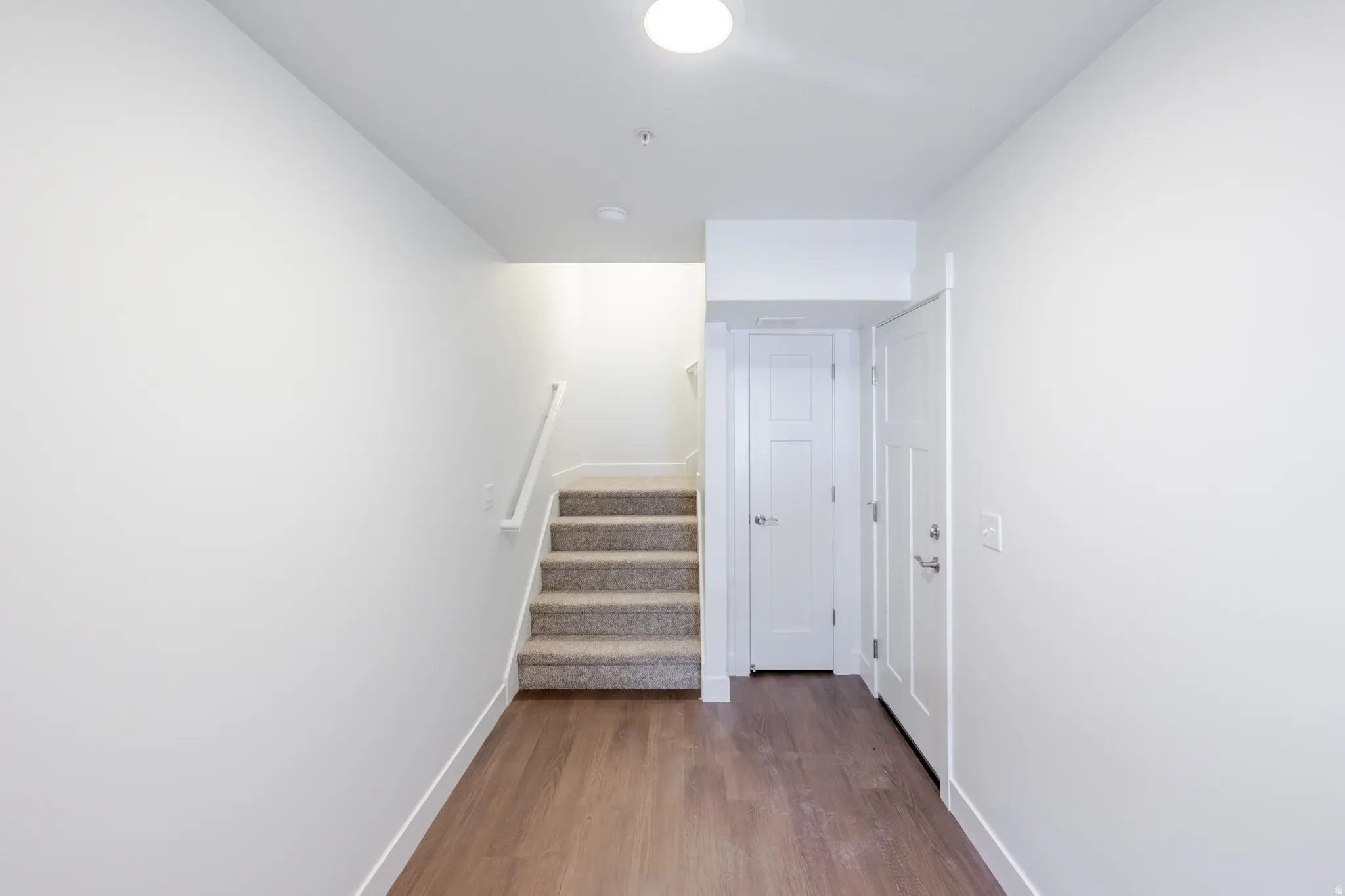 Foyer featuring wood-finish flooring, white trim, and a carpeted staircase with a white handrail