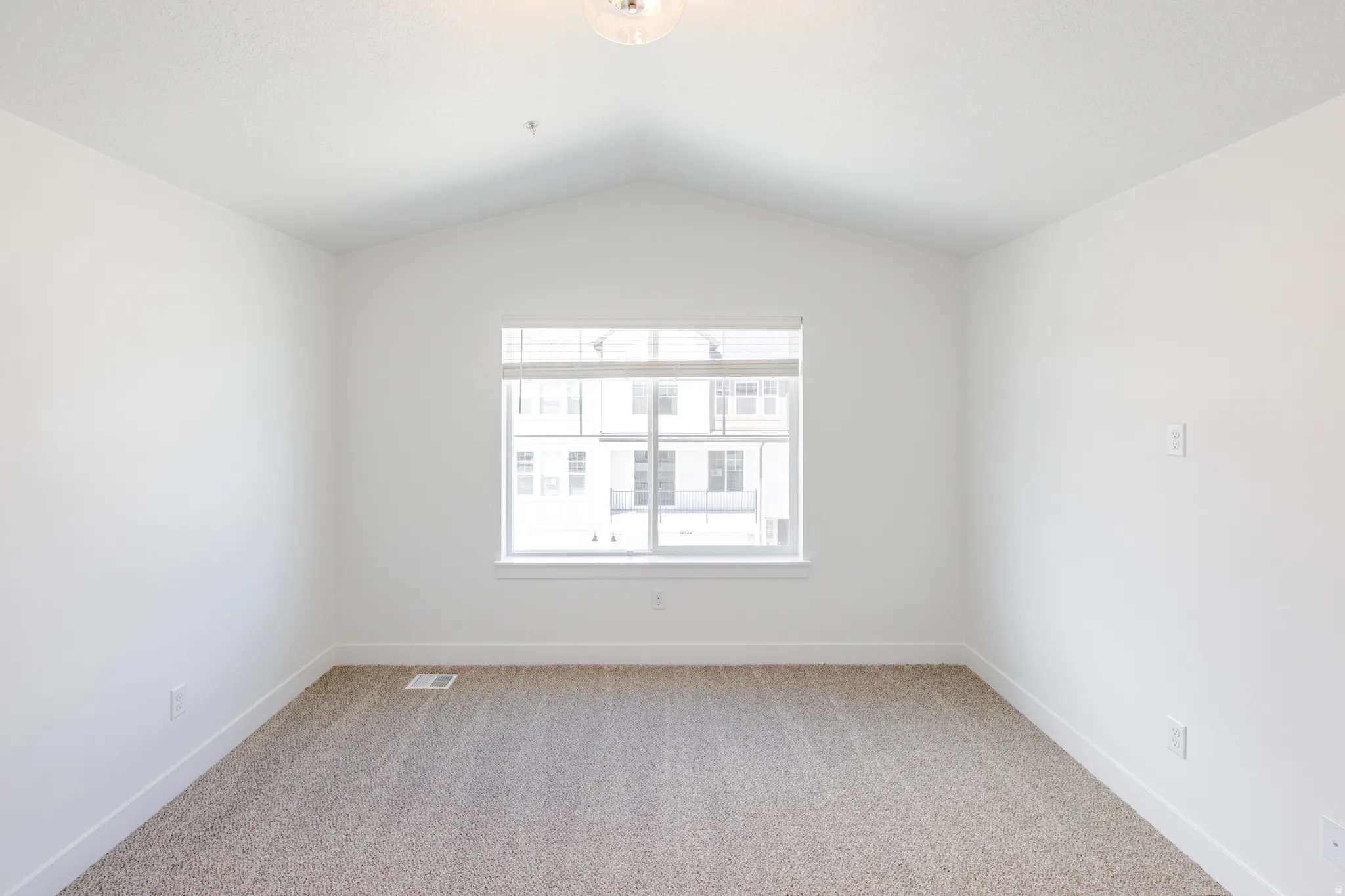 Room featuring a vaulted ceiling, neutral tone carpeting, and white baseboards