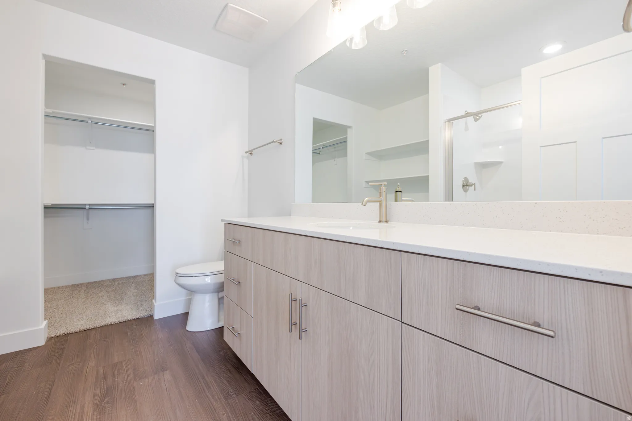 Bathroom featuring a wood-finish double vanity with a light-toned countertop, a large mirror, and a contemporary light fixture