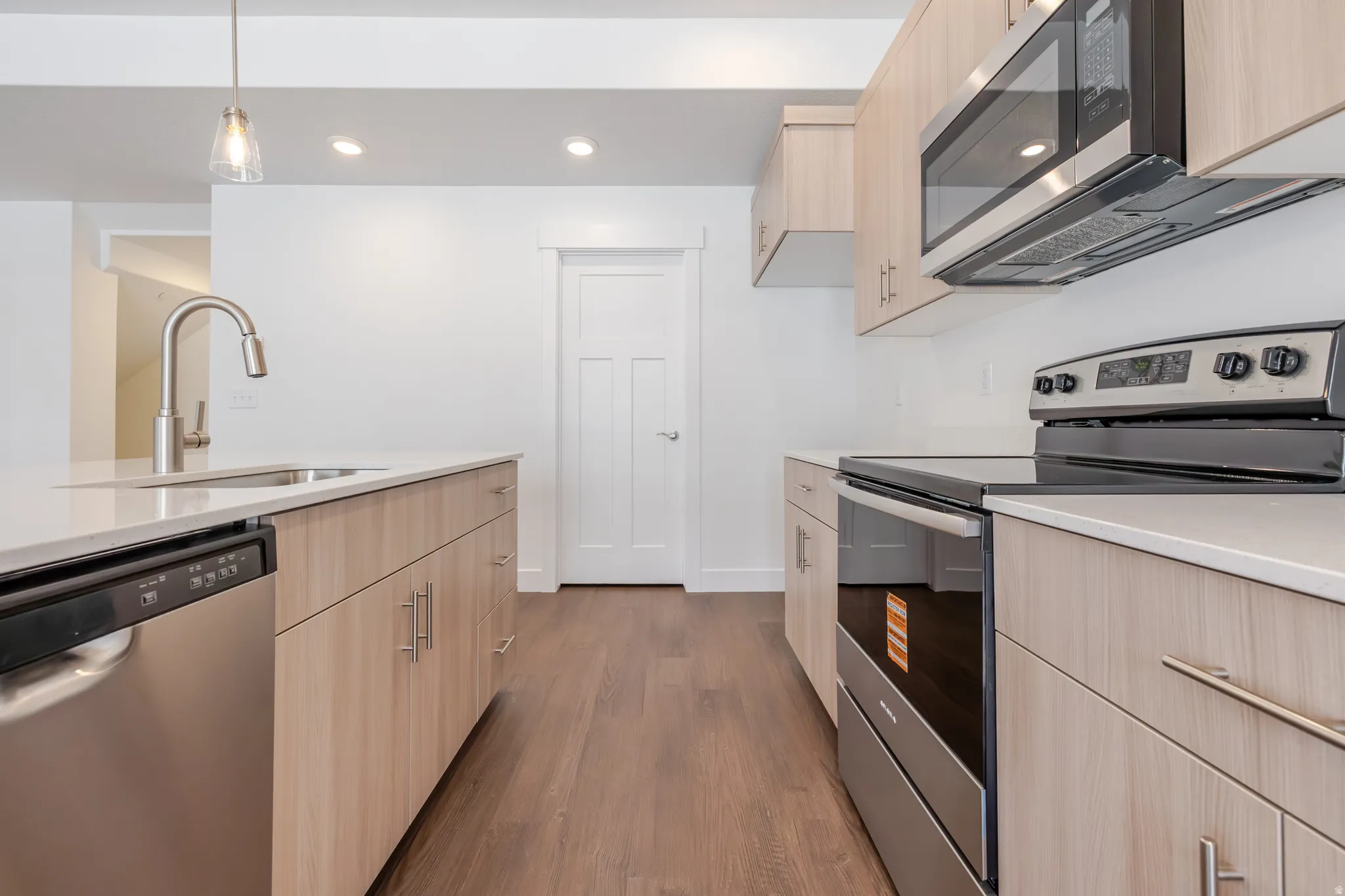Modern kitchen featuring wood-finish cabinetry, light-toned countertops, and stainless steel appliances including a dishwasher, range, and microwave
