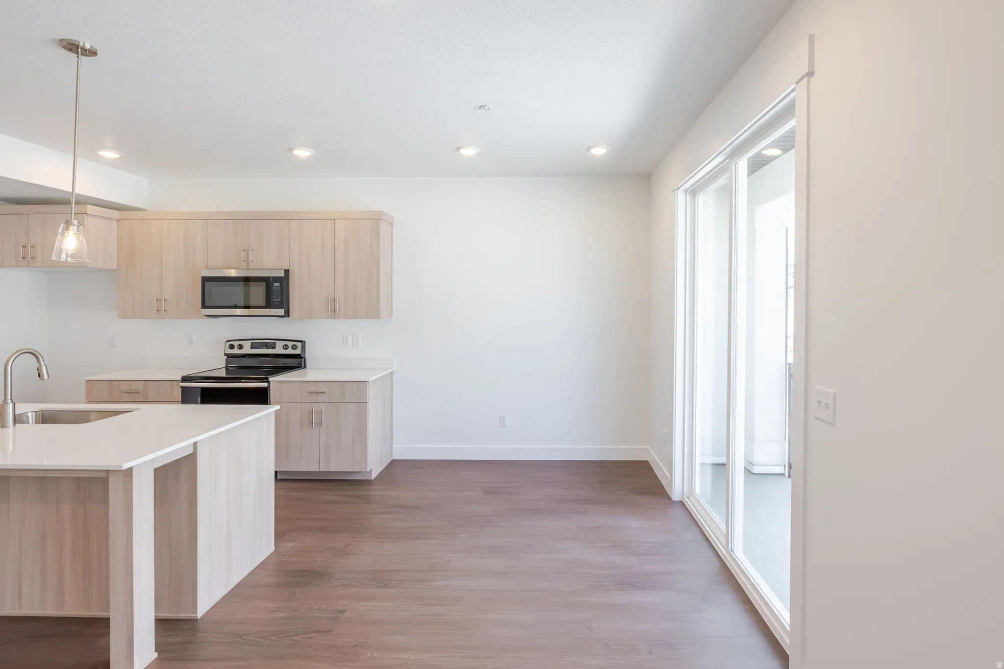 Open-concept kitchen and dining area featuring light wood-finish cabinetry, stainless steel appliances, a kitchen island with an undermount sink, recessed lighting, and wood-finish flooring