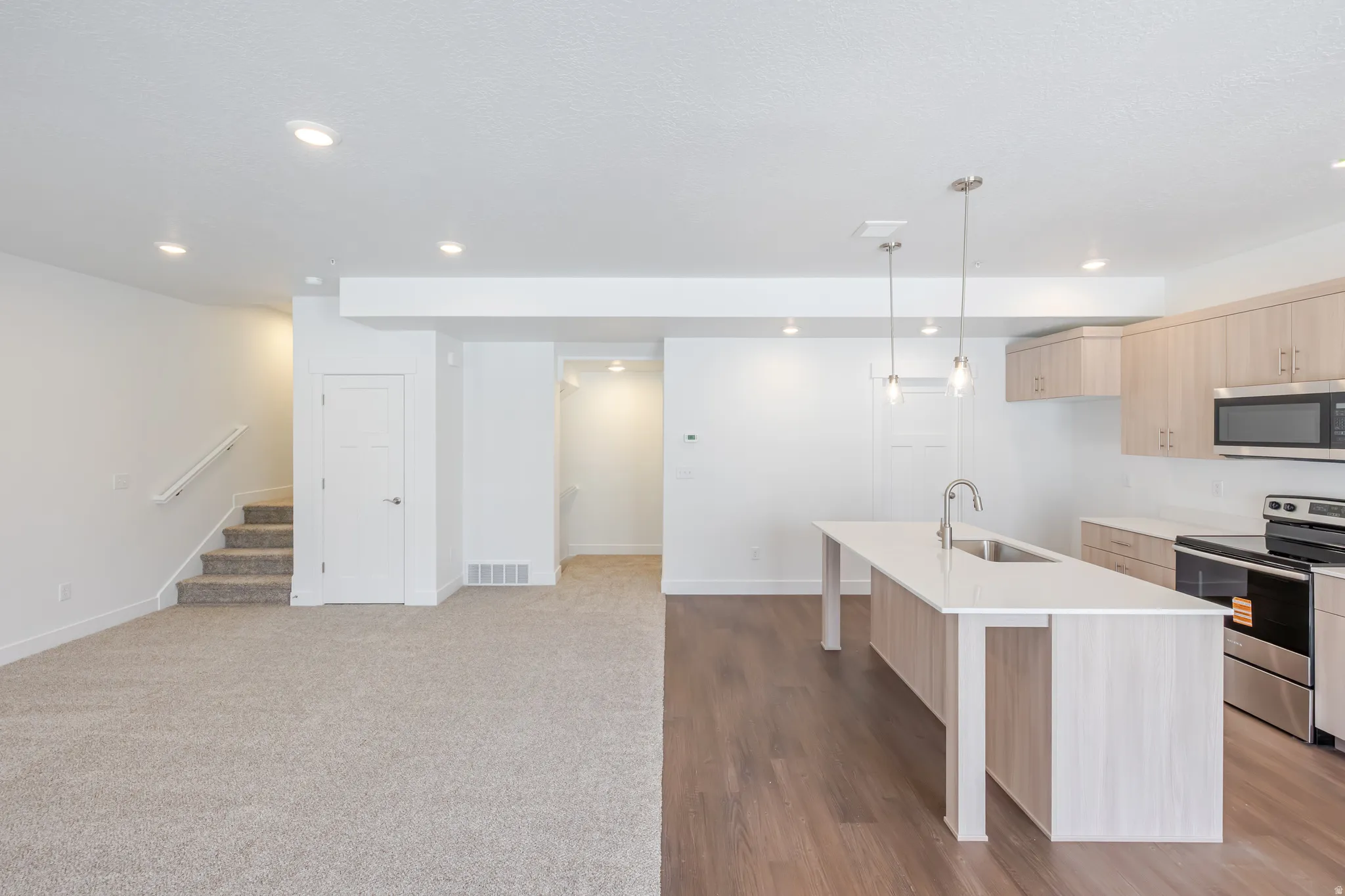 Open-concept space featuring a kitchen with light wood-finish cabinetry, stainless steel appliances, and a central island with a sink and pendant lighting