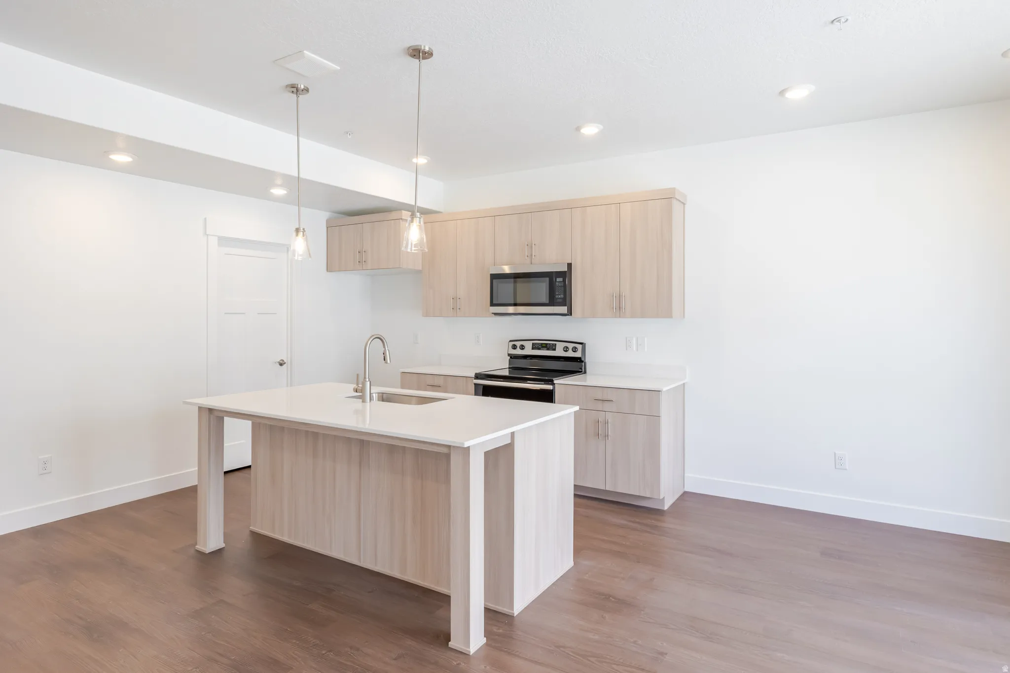 Modern kitchen featuring a central island with an undermount sink, quartz countertops, and light wood-finish cabinetry