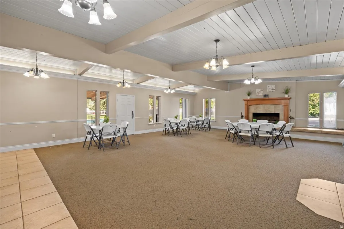 Dining room with suspended lighting, light colored carpet, a fireplace, beamed ceiling, and light tile patterned flooring