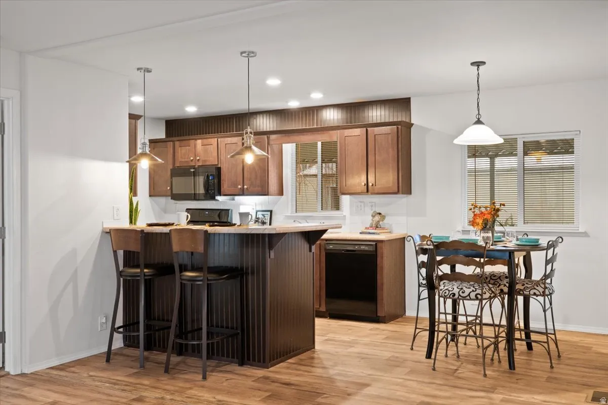 Kitchen with dining area. a peninsula, light countertops, decorative light fixtures, and black appliances