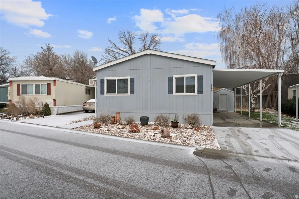 View of front facade featuring concrete driveway, a carport, and a storage shed