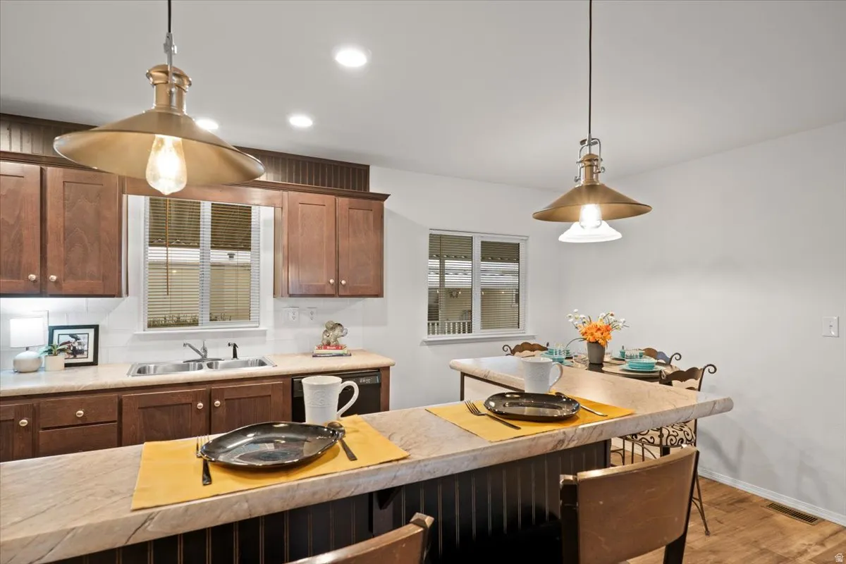 Kitchen with hanging light fixtures, light countertops, dishwasher, a kitchen breakfast bar, and light wood-style flooring