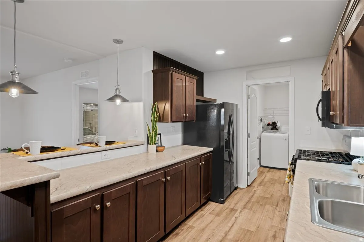 Kitchen with dark brown cabinets, hanging light fixtures, black appliances, light wood-type flooring, and recessed lighting