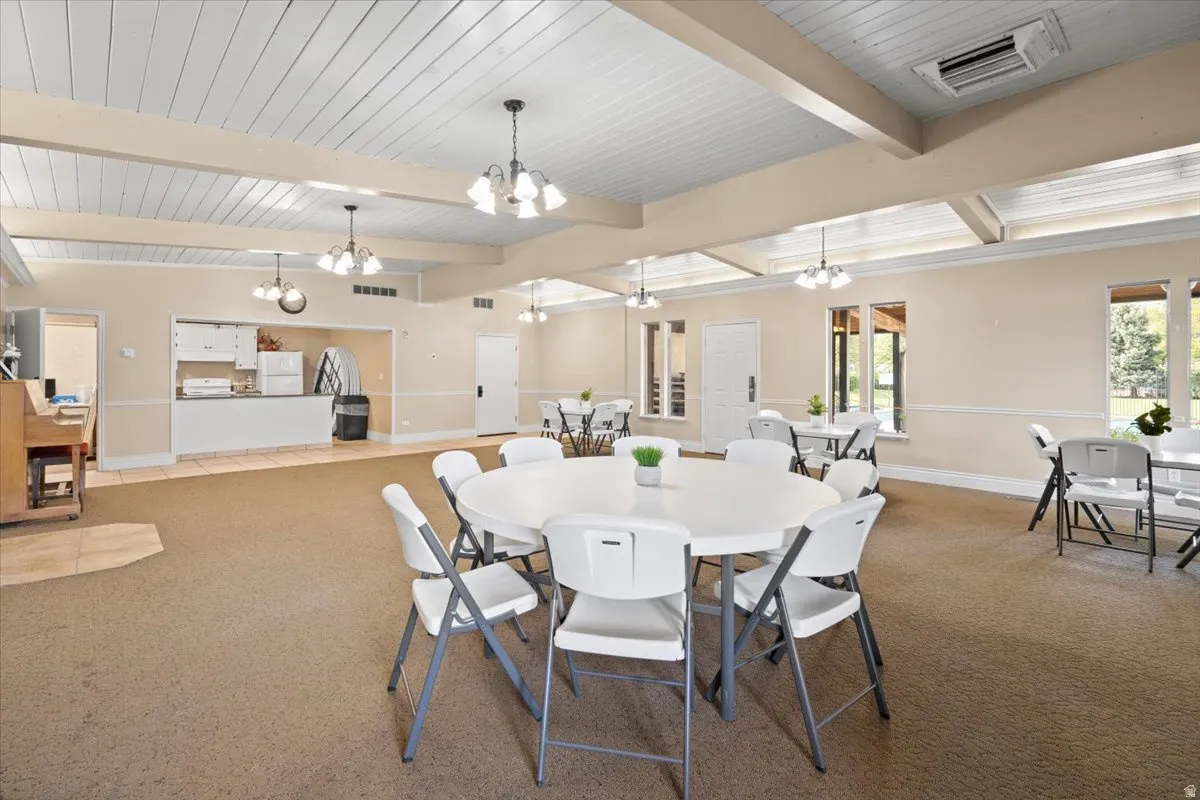 Dining area with carpet flooring, cooling unit, suspended lighting, vaulted ceiling with beams, and wood ceiling