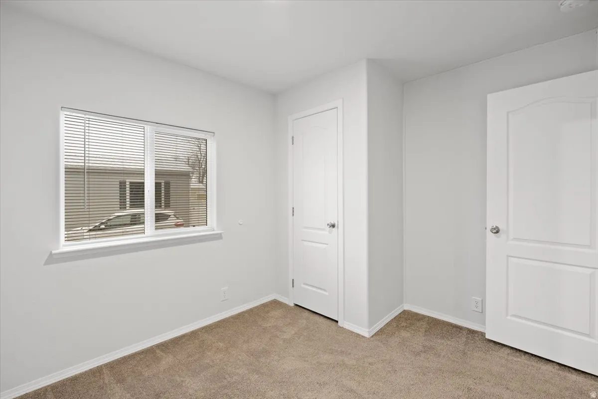 Unfurnished bedroom with light carpet and baseboards