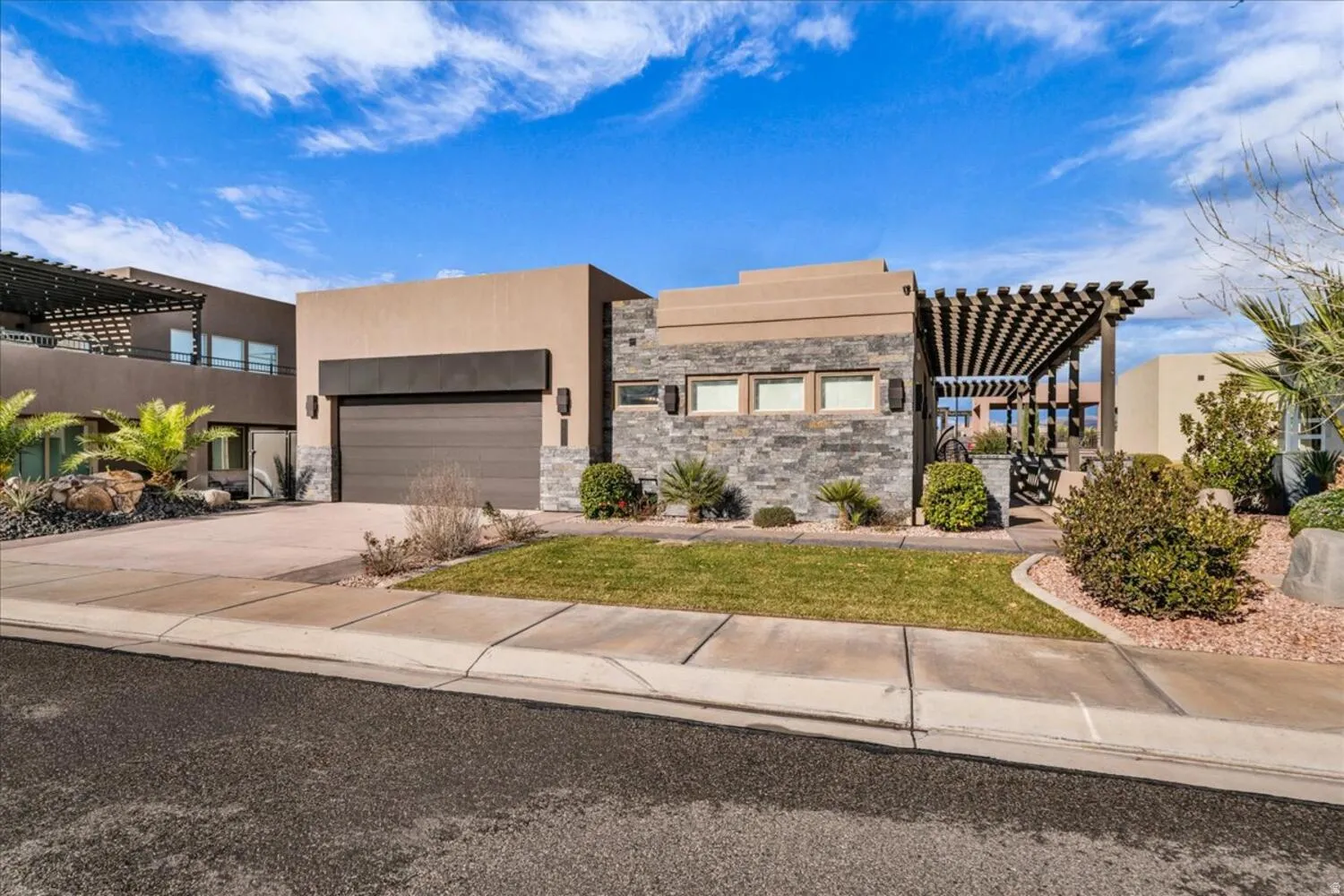 View of front of property with a pergola, stone siding, driveway, and stucco siding