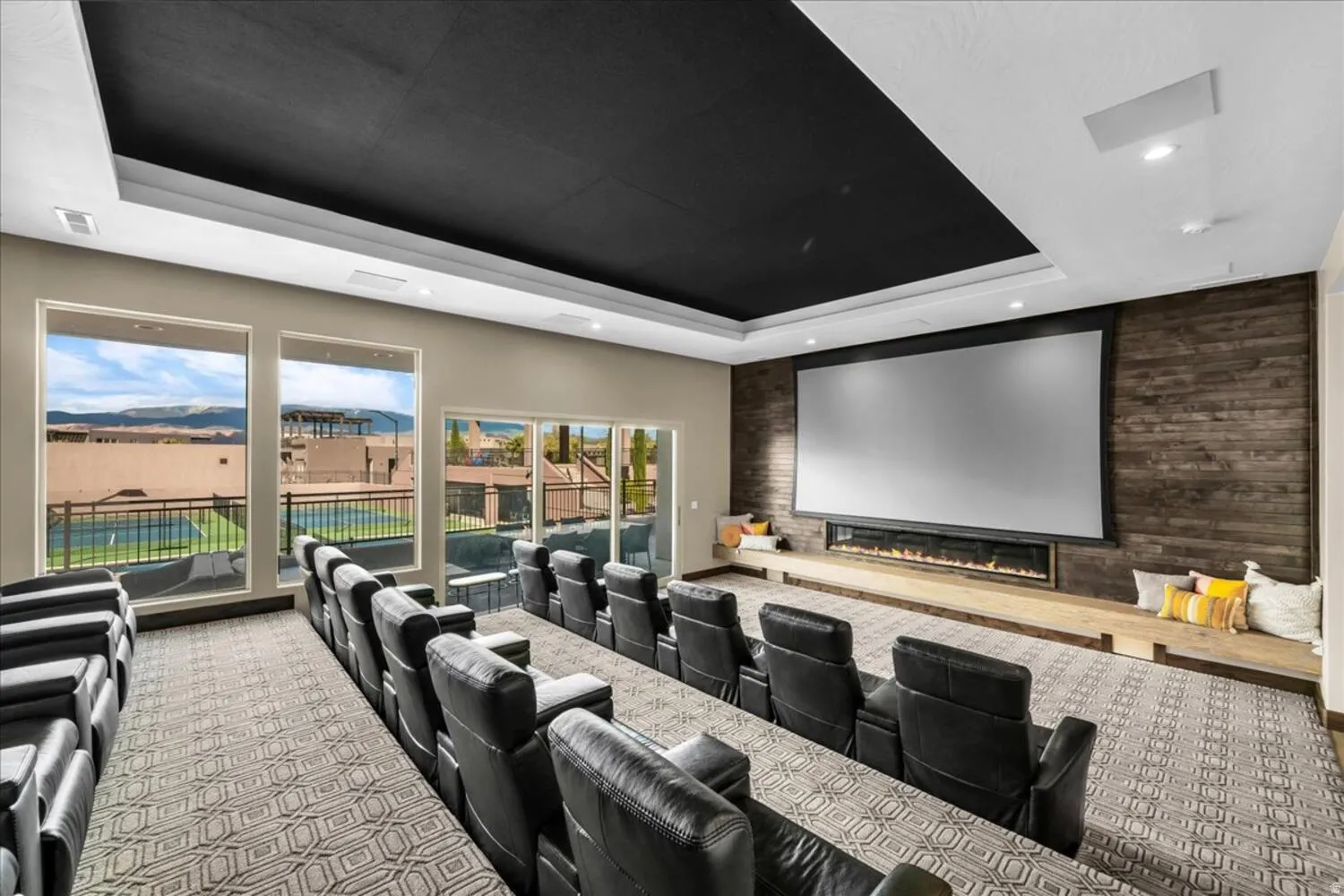 Carpeted cinema room with an accent wall, a raised ceiling, a glass covered fireplace, and recessed lighting