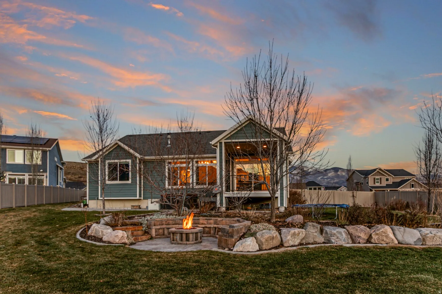 Back of property at dusk with a trampoline, a fenced backyard, a patio area, and a fire pit