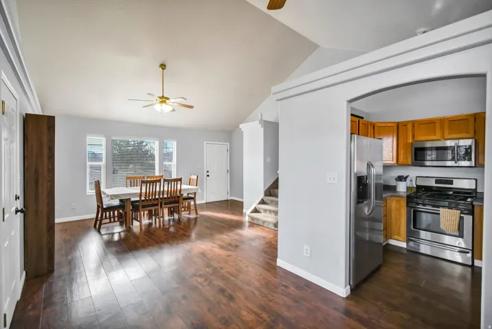 Kitchen featuring ceiling fan, appliances with stainless steel finishes, brown cabinets, dark wood finished floors, and lofted ceiling