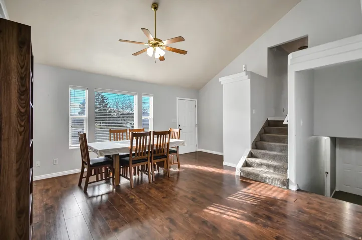 Dining room with stairs, vaulted ceiling, dark wood-style flooring, and a ceiling fan